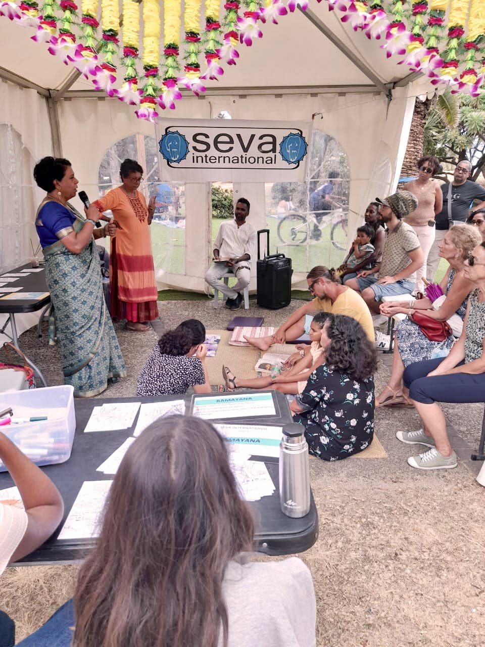 Une intervenante au micro sous le chapiteau SEVA International, devant un public assis
